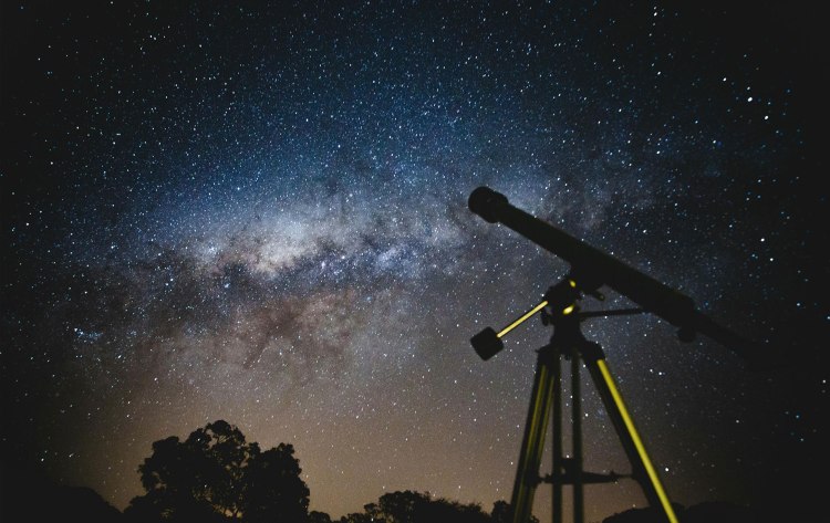The Milky Way Galaxy with a telescope standing in before it.
